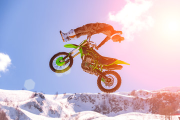 racer on a motorcycle in flight, jumps and takes off on a springboard against the snowy mountains