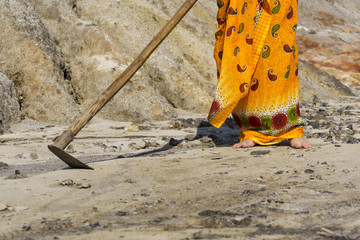 a woman in an ethnic bright dress with a primitive hoe trying to cultivate dry hard barren sandy earth