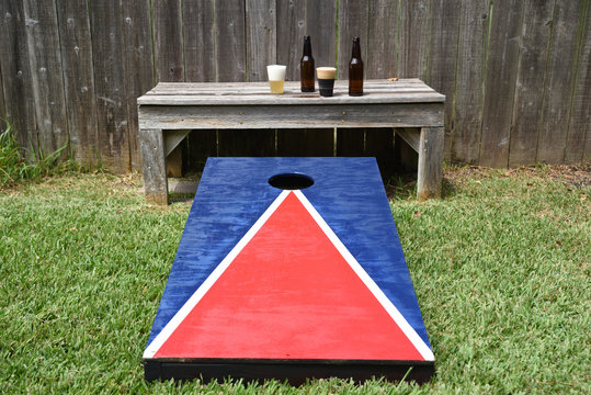 Red, white and blue corn hole game in back yard with dusty bags landing on board