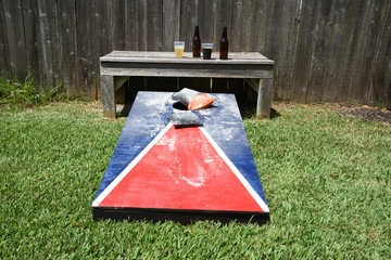Red, white and blue corn hole game in back yard with dusty bags landing on board