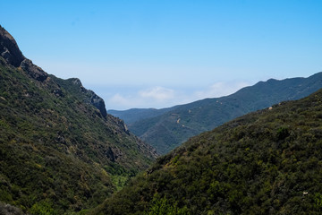Mountains in Malibu, California with a blue sky as fog rolls in on a bright sunny day.