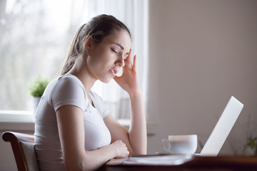 Frustrated young woman working at laptop suffering from severe headache, exhausted female...