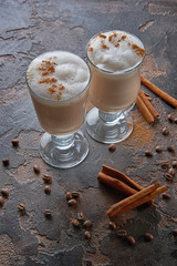 two glasses of latte on a wooden table with coffee beans and cinnamon