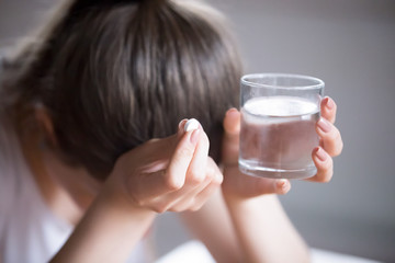Sick frustrated woman feel unwell holding glass of water and pill doubting to take medicine,...
