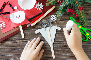 The child glues the parts Christmas Reindeer stics puppets. Handmade. Project of children's...