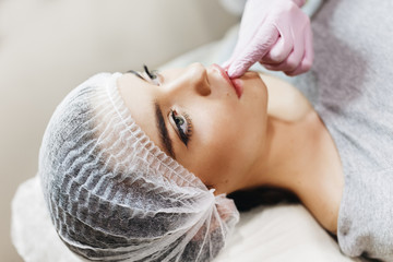 Preparation process for the lip enhancement. The doctor draws up  hyaluronic acid in front of the patient. The young girl with a beautiful face in the special hat and hands of the doctor in pink glove