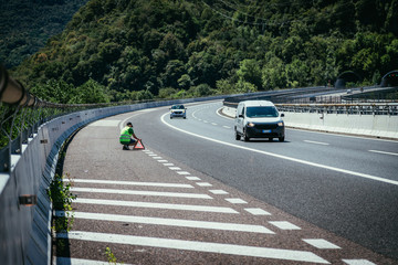 Panne auf der Autobahn: Junger Mann in gelber Warneweste stellt Pannendreieck zur Sicherung auf 