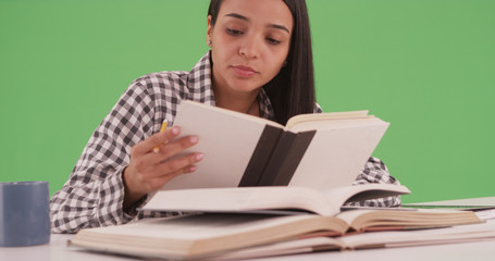 Hispanic college student studying for a final with many books on green screen