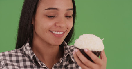 Young hispanic girl eating a coconut cupcake on green screen