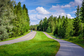 Asphalt road and bike path in Finland. Beautiful summer landscape with forest and blue sky.