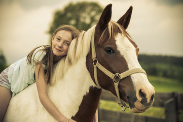Obraz premium Young girl is sitting on a horse / Young girl is sitting on a horse, hugging it and smiling at the camera.