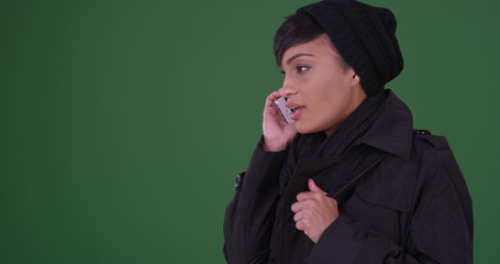 Black woman in black overcoat talking on cellphone on green screen