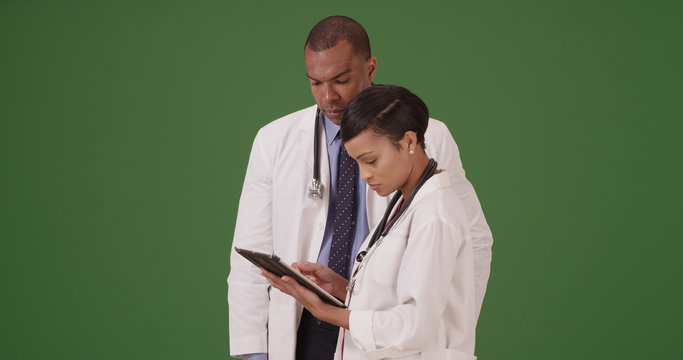 Two Black Medical Professionals Reviewing Data On Tablet Device On Green Screen