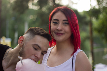 young happy couple girl with red hair guy with beard in park eating sweet cotton