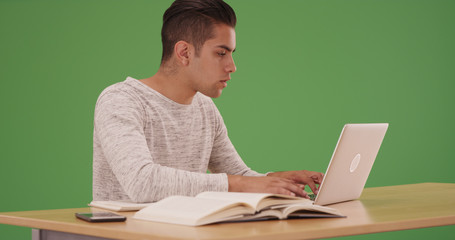 Millennial Hispanic university student working on laptop on green screen