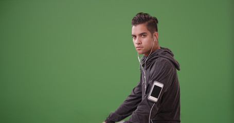 Latino runner wearing hoodie and smartphone with earbuds resting on green screen