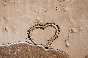 emblem of the heart of love is painted on the sea sand on a warm summer day next to the prints of human feet