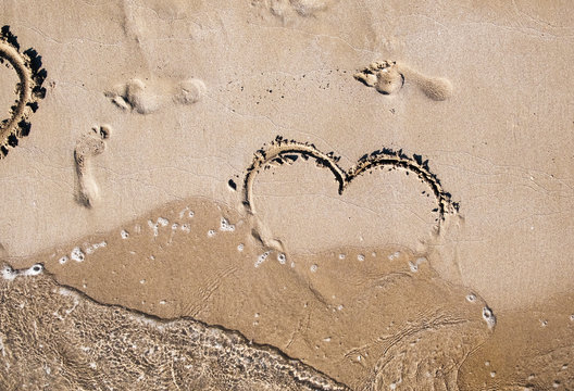 emblem of the heart of love is painted on the sea sand on a warm summer day next to the prints of human feet