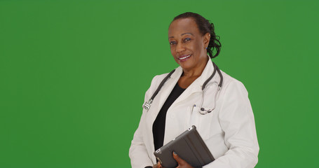 An older black doctor posing for a portrait in with tablet on green screen - Powered by Adobe