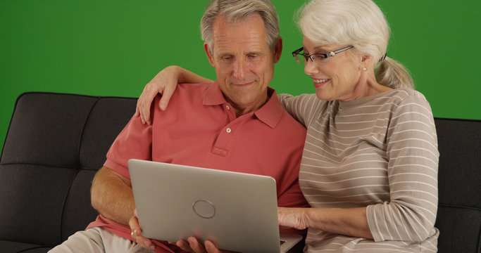 Old white couple watching movie on laptop at home on green screen