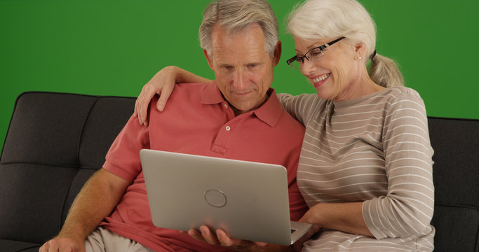 White elderly couple using laptop together at home on green screen