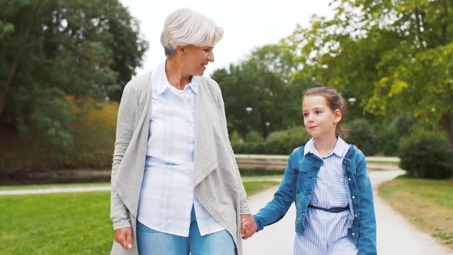 family, leisure and people concept - happy grandmother and granddaughter walking at summer park