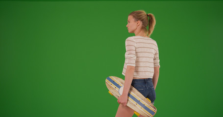 Young millennial female skater with skateboard standing on green screen