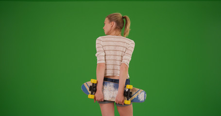 Rear view of skater girl with skateboard waiting for friends on green screen © Mark Adams