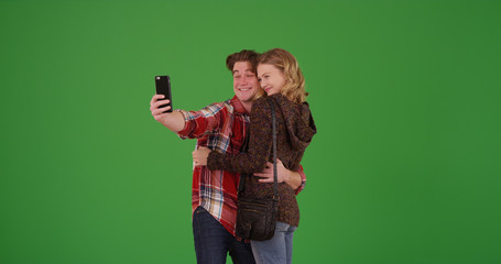 Young millennial couple posing for smartphone selfie together on green screen