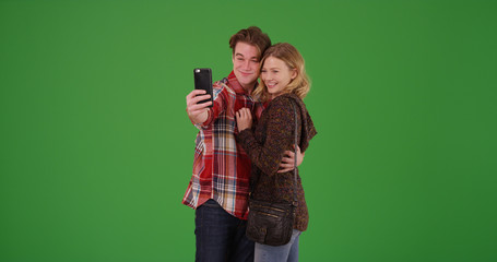 Young millennial couple taking selfies together with cellphone on green screen
