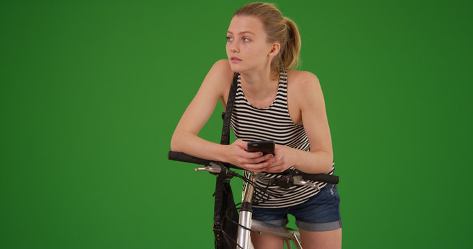 Young lady out on bike ride taking break to text on phone on green screen