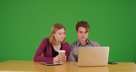 Male and female coworkers watching video on laptop together on green screen