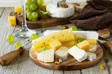 Assortment of cheeses, wine glass and nuts on a wooden table.
