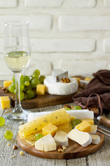 Cheese plate with grapes,  wine glass and nuts on a wooden table. Copy space.