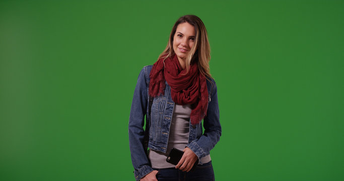 Portrait of smiling stylish millennial girl with phone posing on green screen