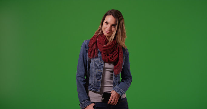 Smiling woman wearing denim jacket and scarf standing with phone on green screen