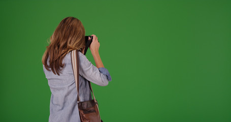 Rear view of blonde woman taking photo with camera on green screen
