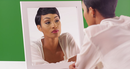 Lovely black woman looking at her reflection in mirror on green screen