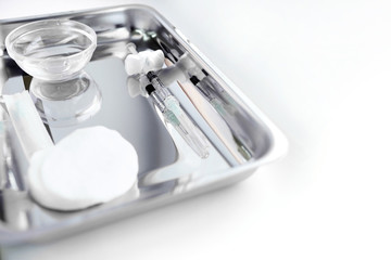 A new syringe filled with a medical product and lying on a silver tray. Tools for the procedure of...