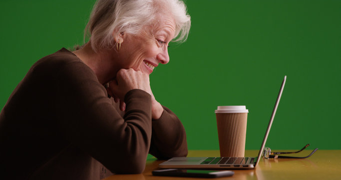 Side view of happy senior businesswoman using laptop on green screen