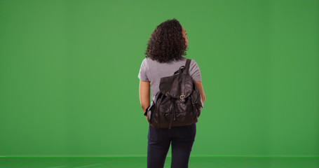 Rear view of African American woman wearing backpack standing on green screen - Powered by Adobe