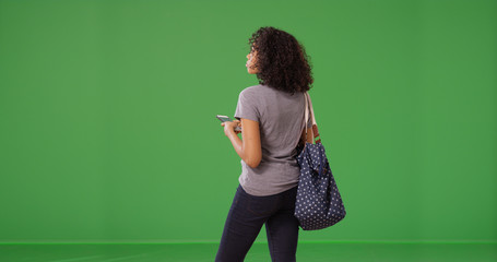 Rear view of black woman texting on smartphone on green screen