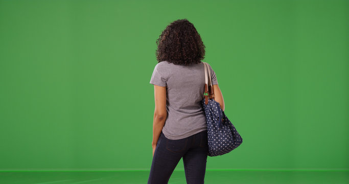 Rear view of young black woman standing holding purse on green screen