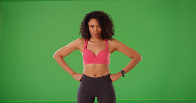 Confident black female with hands at hips in sportswear posing on green screen
