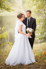 Happy wedding couple. Bride and groom are embracing in the park against the background of the pond....