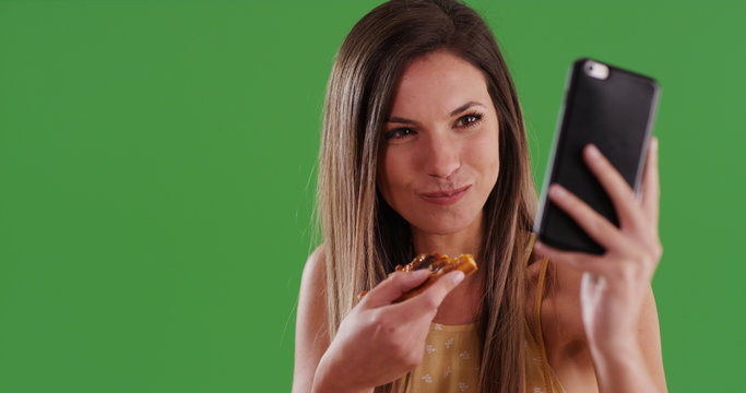 Young millennial white woman taking selfie while eating pizza on green screen