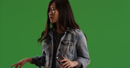 Asian female with earbuds on listening to music grooving on green screen