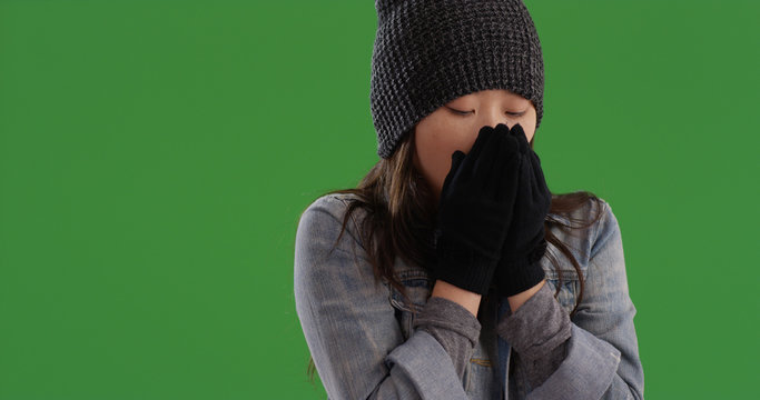 Cold Asian woman trying to keep warm with gloves and beanie on green screen
