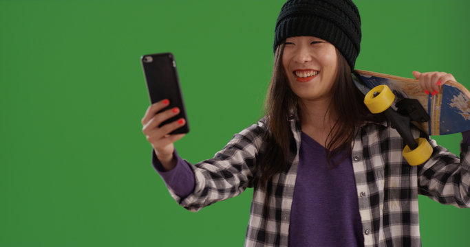 Portrait of happy skater girl taking selfies with smartphone on green screen