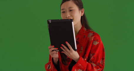 Chinese female in traditional dress watching something on tablet on green screen